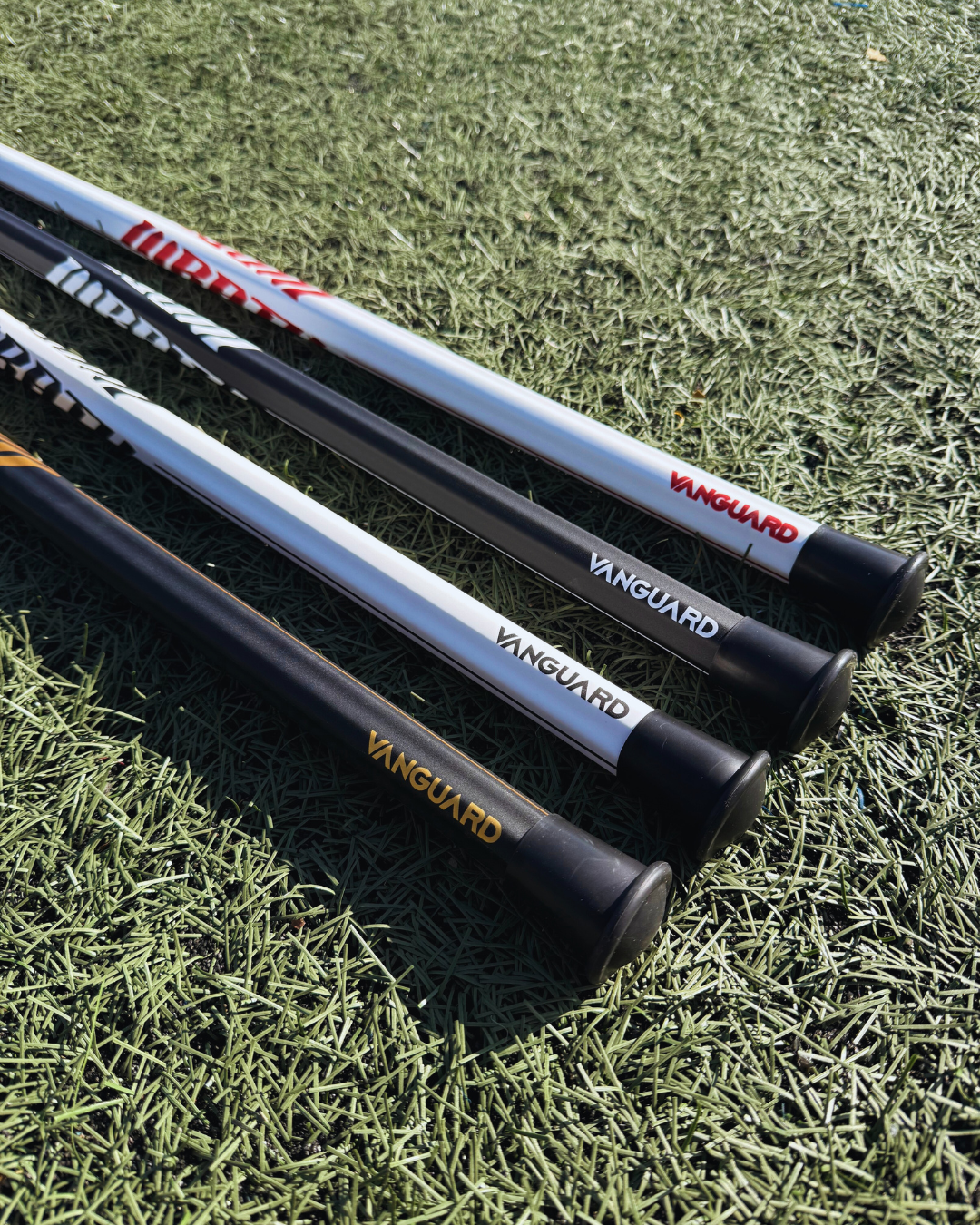 4 lacrosse sticks lying on grass with visible brand logos.