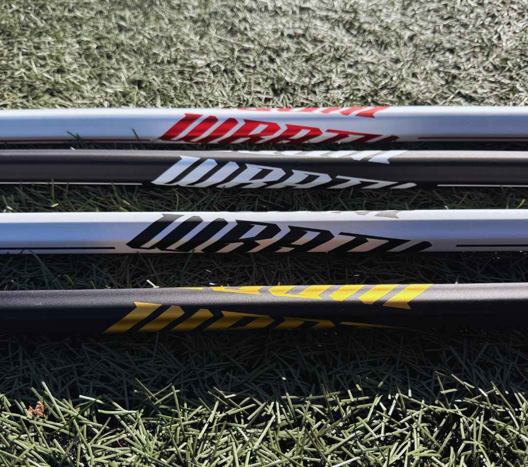 4 lacrosse sticks lying on grass with visible brand logos.