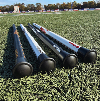 4 lacrosse sticks lying on grass with visible brand logos.