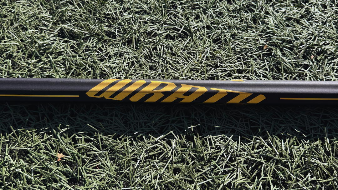 1 lacrosse stick lying on grass with visible brand logos.