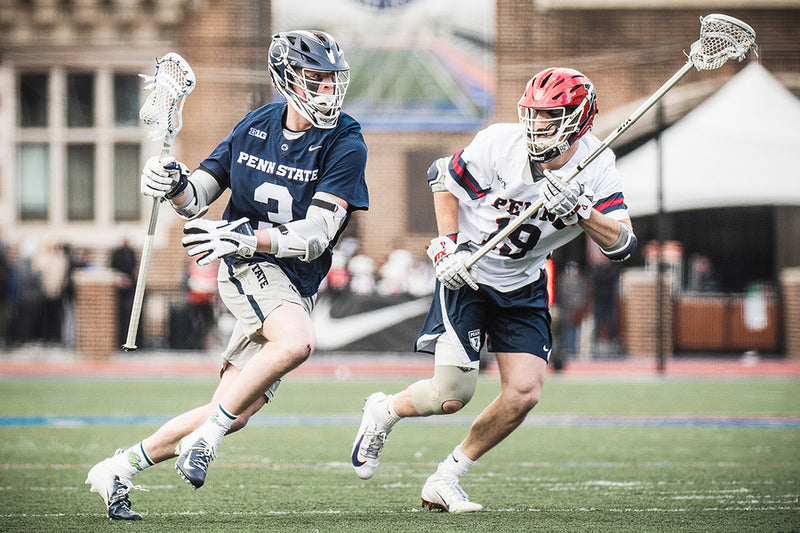 Two lacrosse players in action on a field with 'Penn State' and 'Colgate' jerseys.