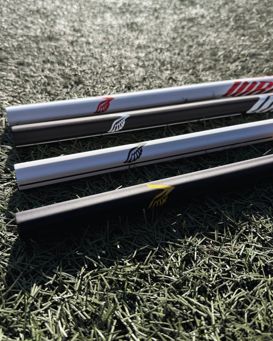 4 lacrosse sticks lying on grass with visible brand logos.